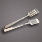Stainless steel tongs for food handling on gray background.