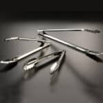 Stainless steel tongs on a dark surface, ideal for food handling and hygiene.
