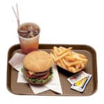 Burger with lettuce, tomato, cheese, French fries, soda, and sauces on a brown tray.