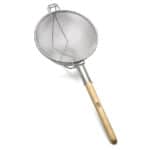 Stainless steel fine mesh skimmer with wooden handle, used in professional kitchen and food hygiene cleaning.