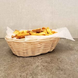 Crispy French fries in a woven basket on a gray surface with a neutral background.