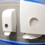 Dispenser and toilet paper holder mounted on a wall in a hygiene or restroom setting, emphasizing sanitation solutions.