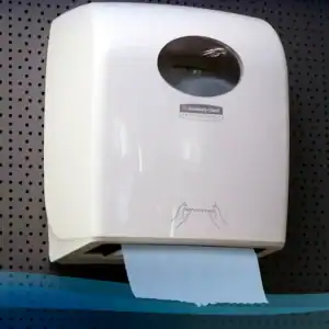 Kimberly-Clark professional paper towel dispenser on a black dotted wall for hygiene and sanitation.