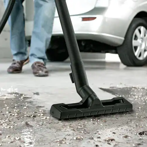 4039784943544 Optimally developed Floor nozzle and suction hose Powerful industrial vacuum cleaner cleaning debris from a rough concrete surface at a construction site. Focus on durability and high performance for effective industrial cleaning solutions.