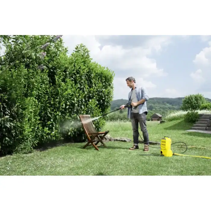Pressure washing outdoor garden furniture with a power washer in lush green garden.