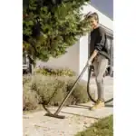 Vacuum cleaner in outdoor garden, woman cleaning pathway with handheld vacuum, professional cleaning service, Beyond Hygiene Asia, urban outdoor cleaning, efficient carpet and floor cleaning equipment.