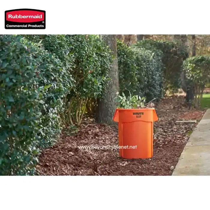 Orange trash bin for yard waste collection with gardening debris, positioned outdoors near a landscaped hedge and trees, promoting proper waste disposal and outdoor cleanliness.