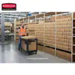 Bright warehouse worker in safety vest organizing parcels on a trolley amidst neatly stacked cardboard boxes, emphasizing efficient logistics and inventory management for hygiene and sanitation supplies.