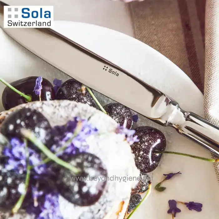 Cherry pie with fresh cherries, purple flowers, and powdered sugar, with a Swiss Sola knife on a white surface. Perfect for showcasing high-quality kitchen tools and gourmet desserts.