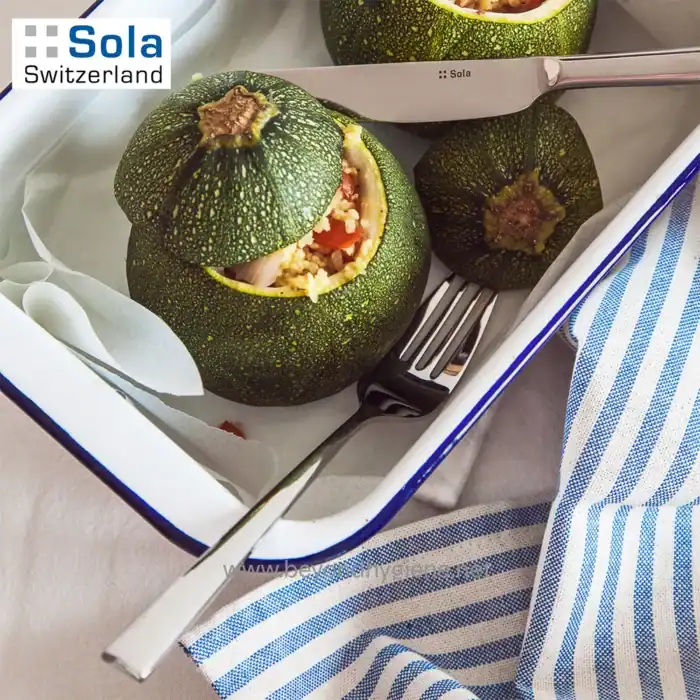 Zucchini stuffed with vegetables on a white tray, with cutlery and a blue-striped cloth, highlighting food presentation and kitchen tools.