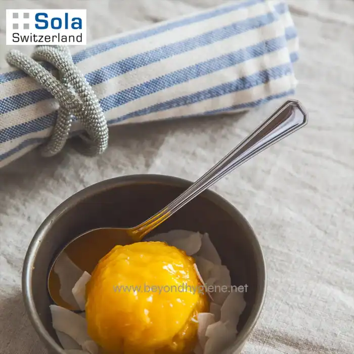 Soft-boiled egg with coconut flakes and a spoon in a metal bowl, placed on a textured cloth surface, with a striped fabric and jewelry in the background.