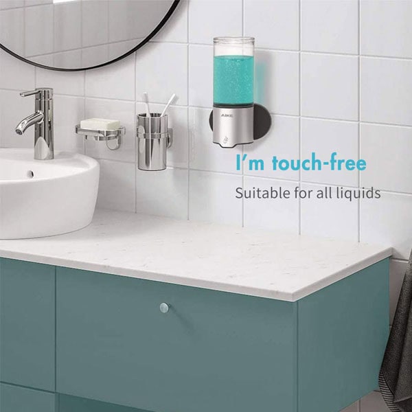 product_20211001-075609_6156bf19c9017 Touchless soap dispenser mounted on a white tiled bathroom wall, with a sink and mirror in the background, promoting hygienic, touch-free liquid dispensing solutions.