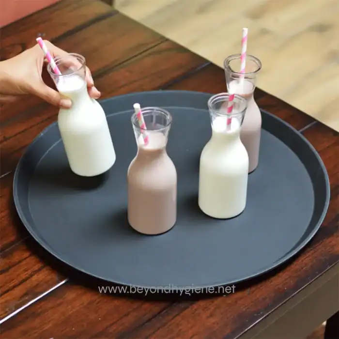 Milk bottles with straws on a black tray, served for a beverage drink, in a hygienic and clean setting.