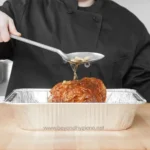 Savory glazed meatloaf being served with gravy in a disposable aluminum tray, emphasizing hygienic food services and Asian cuisine.