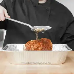 Savory glazed meatloaf being served with gravy in a disposable aluminum tray, emphasizing hygienic food services and Asian cuisine.