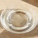 Clear glass ashtray filled with water on wooden surface.