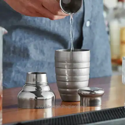 Hand pouring water into metal tumbler at Beyond Hygiene Asia, showcasing professional hygiene solutions and premium drinkware for hospitality and commercial spaces.