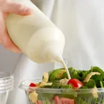 Cream being poured over a fresh salad with tomatoes, greens, and chicken from Beyond Hygiene Asia, highlighting food hygiene and safety standards.