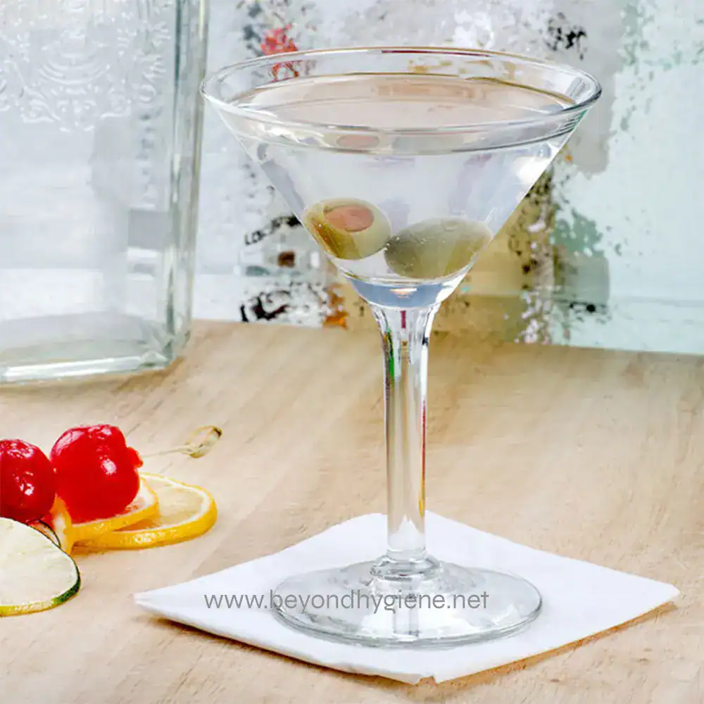391381 Clarity martini with olives and lemon garnish on a wooden table, showcasing clean and hygienic beverage presentation in a professional setting.