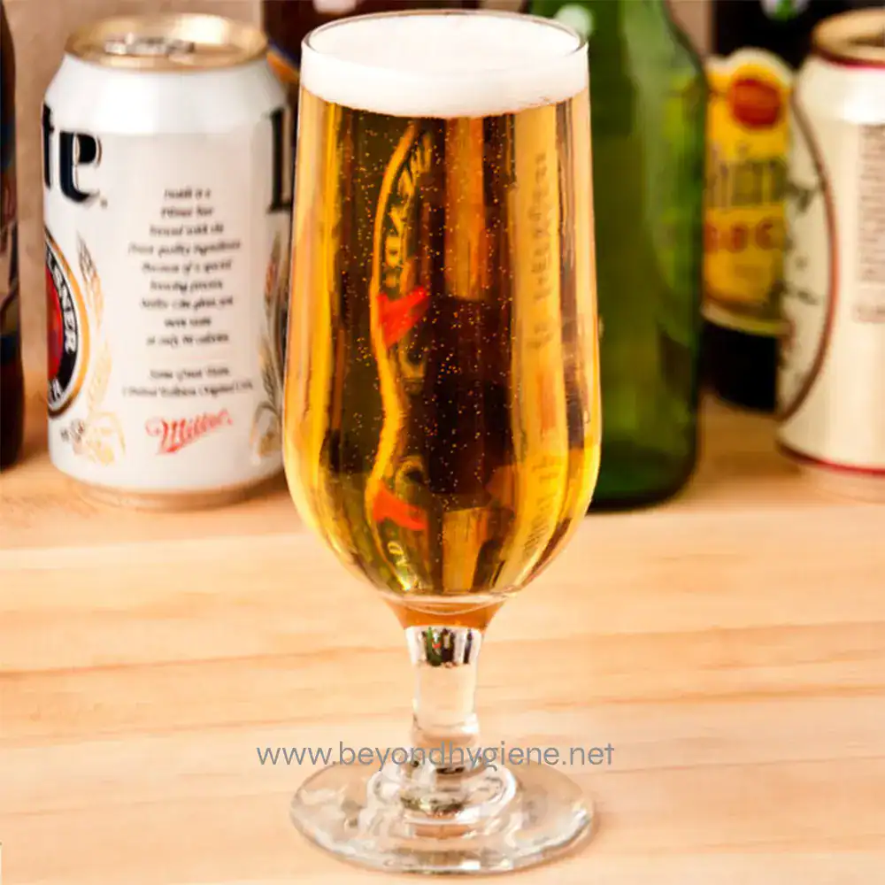 Sparkling beer in a tall glass with foamy head, surrounded by beer cans and bottles, perfect for promoting beer hygiene and cleanliness in hospitality environments.