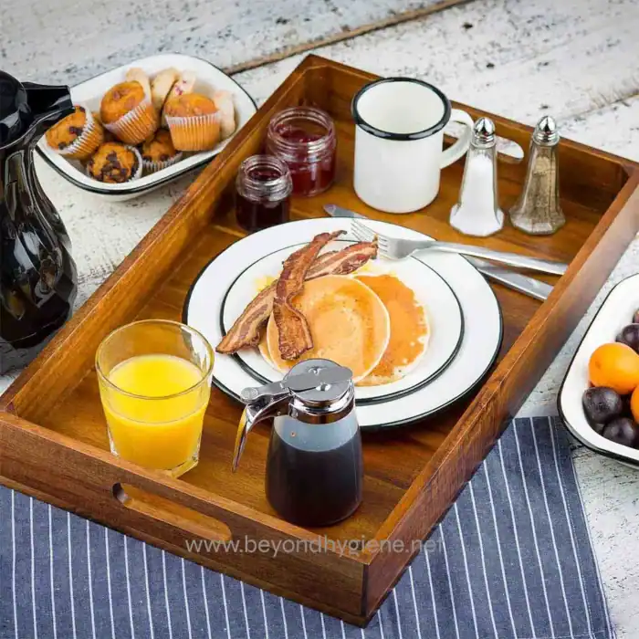 Steak and eggs breakfast served on a wooden tray with orange juice, bacon, pancakes, and condiments for a hearty morning meal.