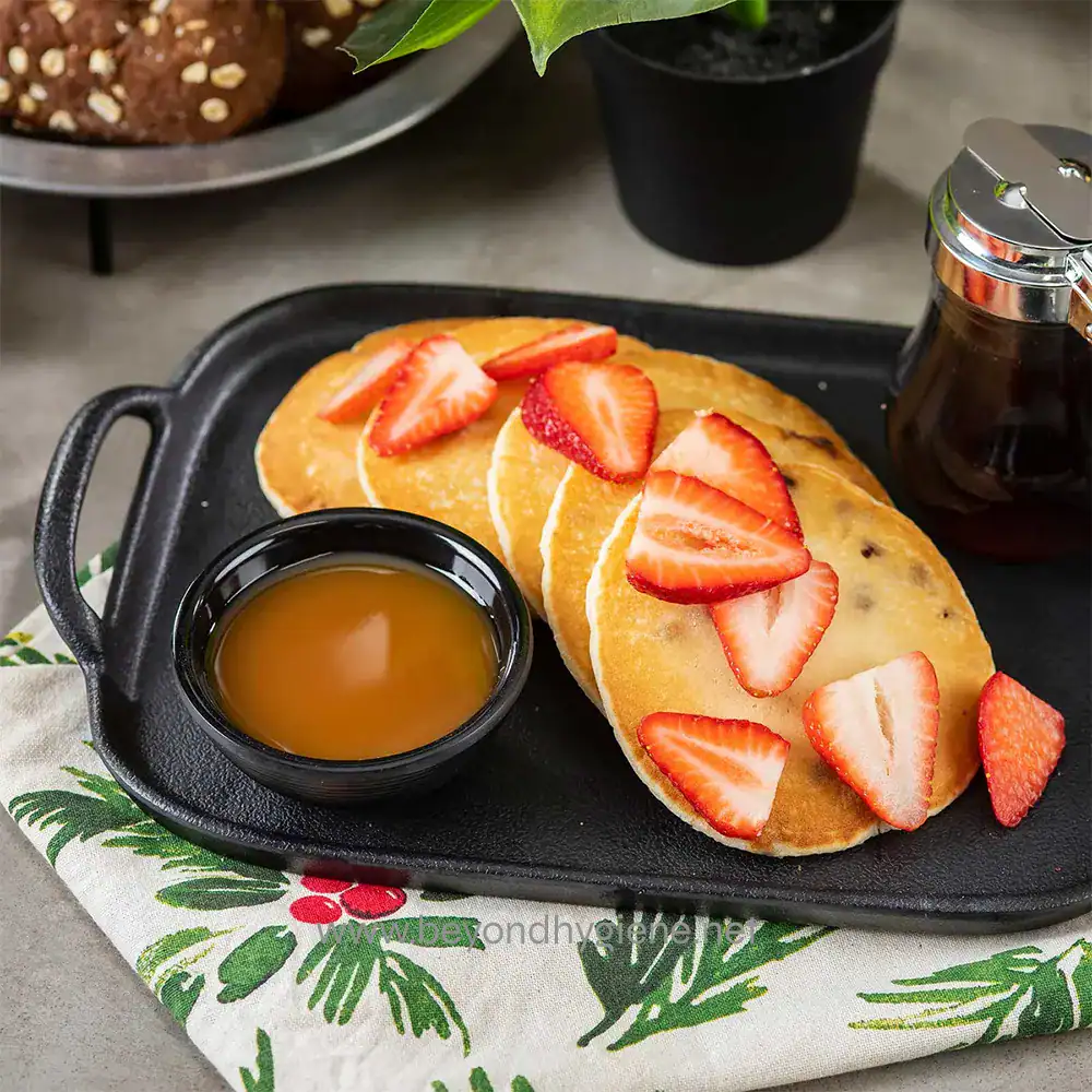 5 Strawberry-topped pancakes with syrup and honey served on a sizzling black platter, perfect for breakfast or brunch, emphasizing delicious food presentation for Beyond Hygiene Asia.