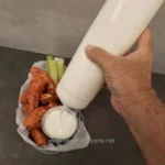 Creamy dipping sauce being poured from a squeeze bottle alongside chicken wings and celery sticks - food presentation, hygiene, and condiment serving.