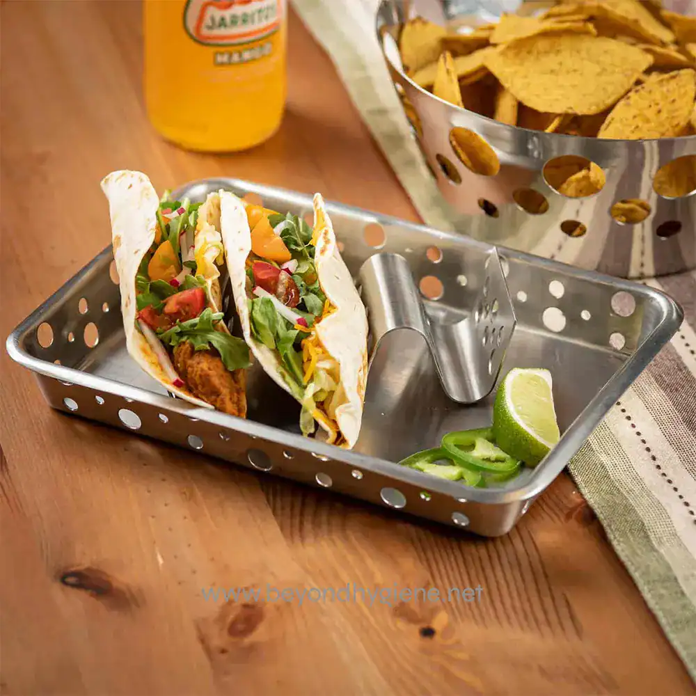 6 Tacos with fresh vegetables and crispy chips served on a metal tray, lime wedges and hot sauce on a wooden table - clean eating and food hygiene.