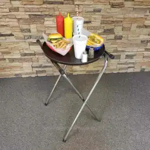 Fresh fast-food meal on a black round tray with ketchup, mustard, salt, pepper, and drinks, set against a stone wall background in a casual dining environment.