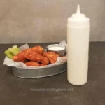 Rich black sauce in glass syrup dispenser with breakfast foods in background, emphasizing hygienic food service.