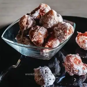 Sugary, powdered donuts dusted with flour in a glass bowl, ready to serve.