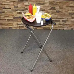 Plastic tray with condiments, ketchup, mustard, and pepper, along with fast food items like fries, burger, and hot dog on a black round table in a casual dining setting.
