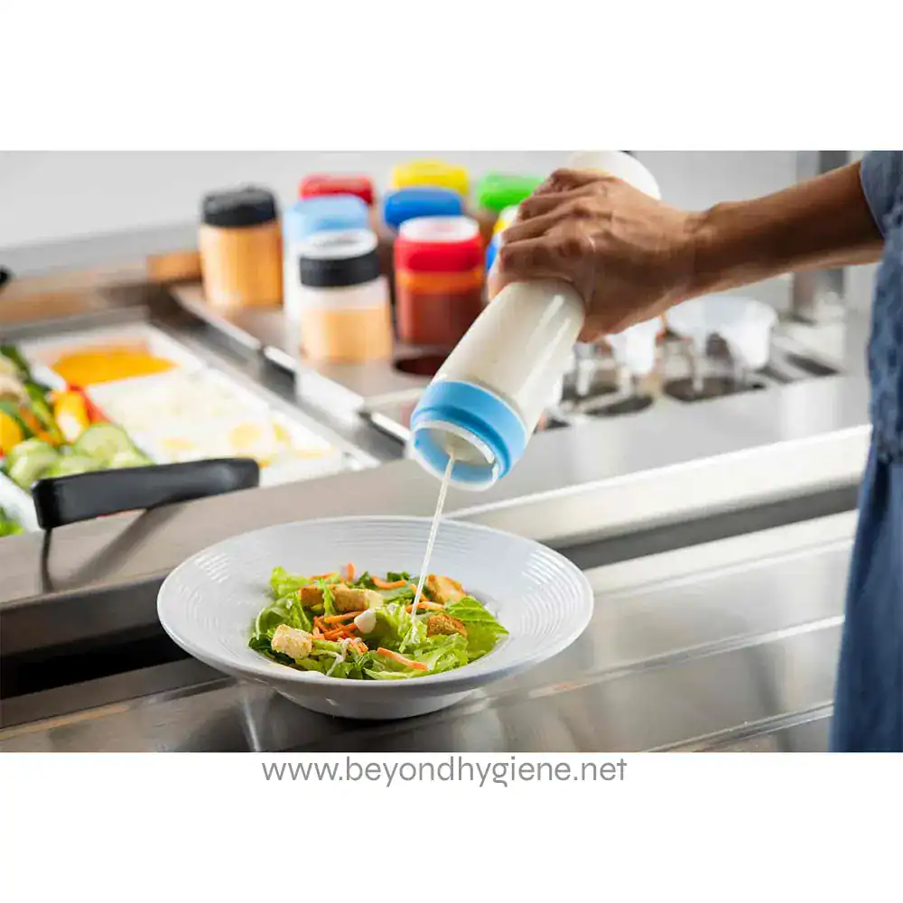 9 Bottle of salad dressing being poured onto a fresh vegetable salad in a professional kitchen setting.
