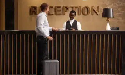 A professional hotel receptionist assisting a guest with luggage at the reception desk.