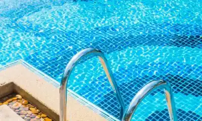 Shiny stainless steel pool ladder next to a sparkling blue tiled swimming pool, highlighting professional pool maintenance and water hygiene services.