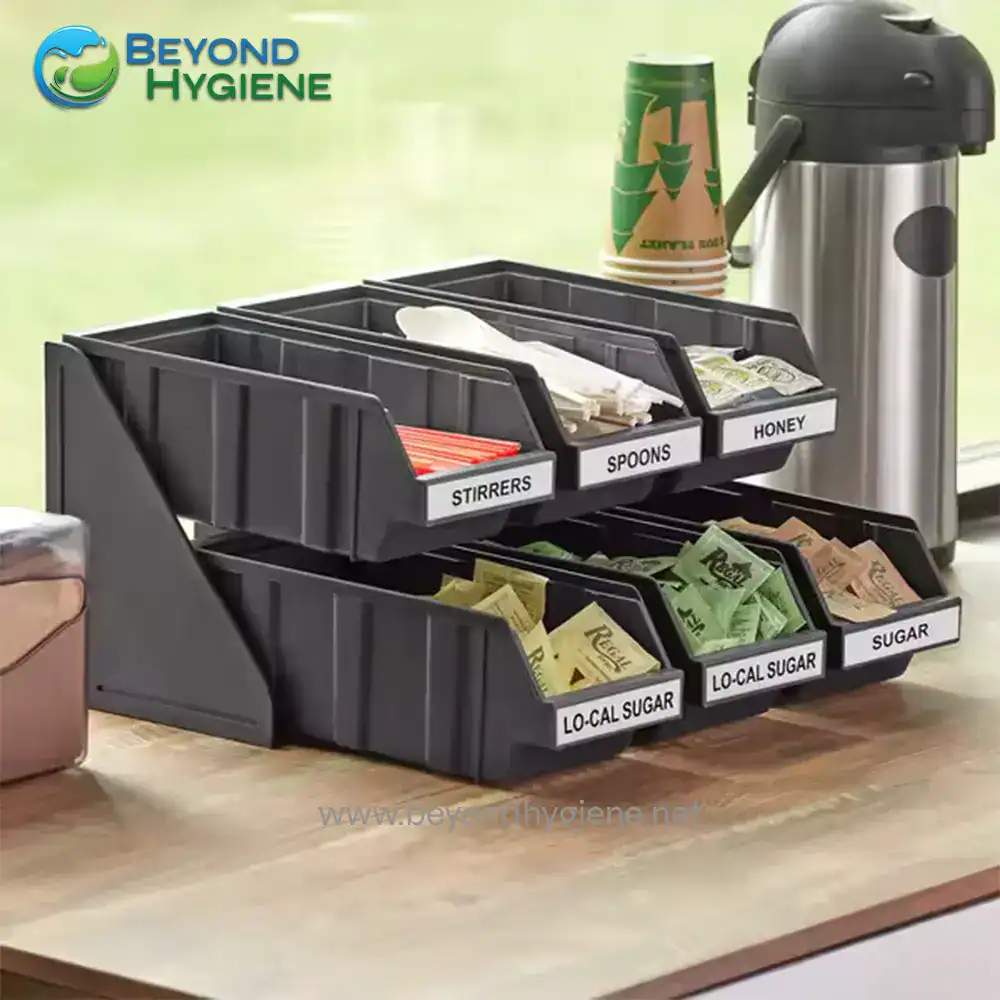 UGA-JD86258A_3 Stainless steel condiment dispenser with labeled compartments for stirrers, spoons, honey, and sugar in a commercial kitchen setting.