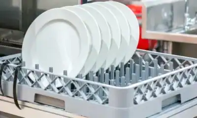 Stacked white ceramic plates on a commercial dishwasher rack, ready for cleaning.