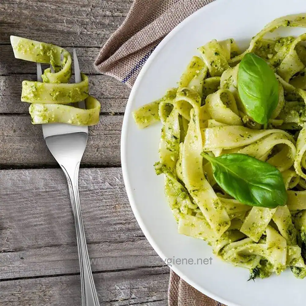 s-l1600 (4) Creamy basil pesto pasta with fresh basil leaves, served on a clean white plate, on rustic wooden surface, showcasing healthy, delicious Italian cuisine from Beyond Hygiene Asia.