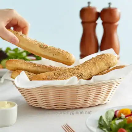 Crusty breadsticks with herbs in a woven basket, ready for serving at a restaurant or home. Perfect for snacks, appetizers, or accompanying meals, emphasizing hygiene and sanitation in food presentation.