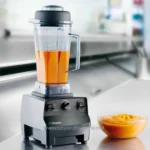 Blender with orange sauce in a commercial kitchen, preparing food for catering or restaurant service, emphasizing hygiene and professional kitchen equipment for food safety and quality.