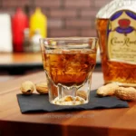 Cold whiskey on the rocks with a blurred background of condiment bottles and nuts, showcasing beverage service and bar hygiene standards.