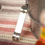 Metal nail clipper next to a metallic container on striped fabric surface.