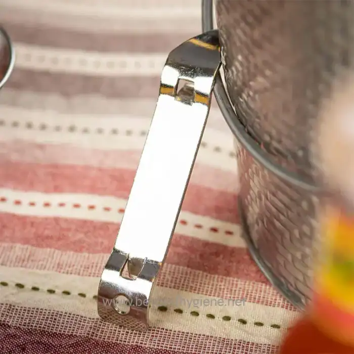 Metal nail clipper next to a metallic container on striped fabric surface.