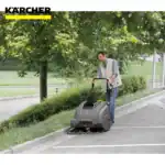 Kärcher industrial floor scrubber cleaning sidewalk outdoors in park area with greenery and trees.