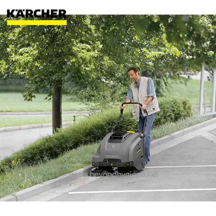 Kärcher industrial floor scrubber cleaning sidewalk outdoors in park area with greenery and trees.