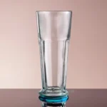 Clear tall drinking glass, perfect for beverages, arranged on a reflective surface with a neutral background.