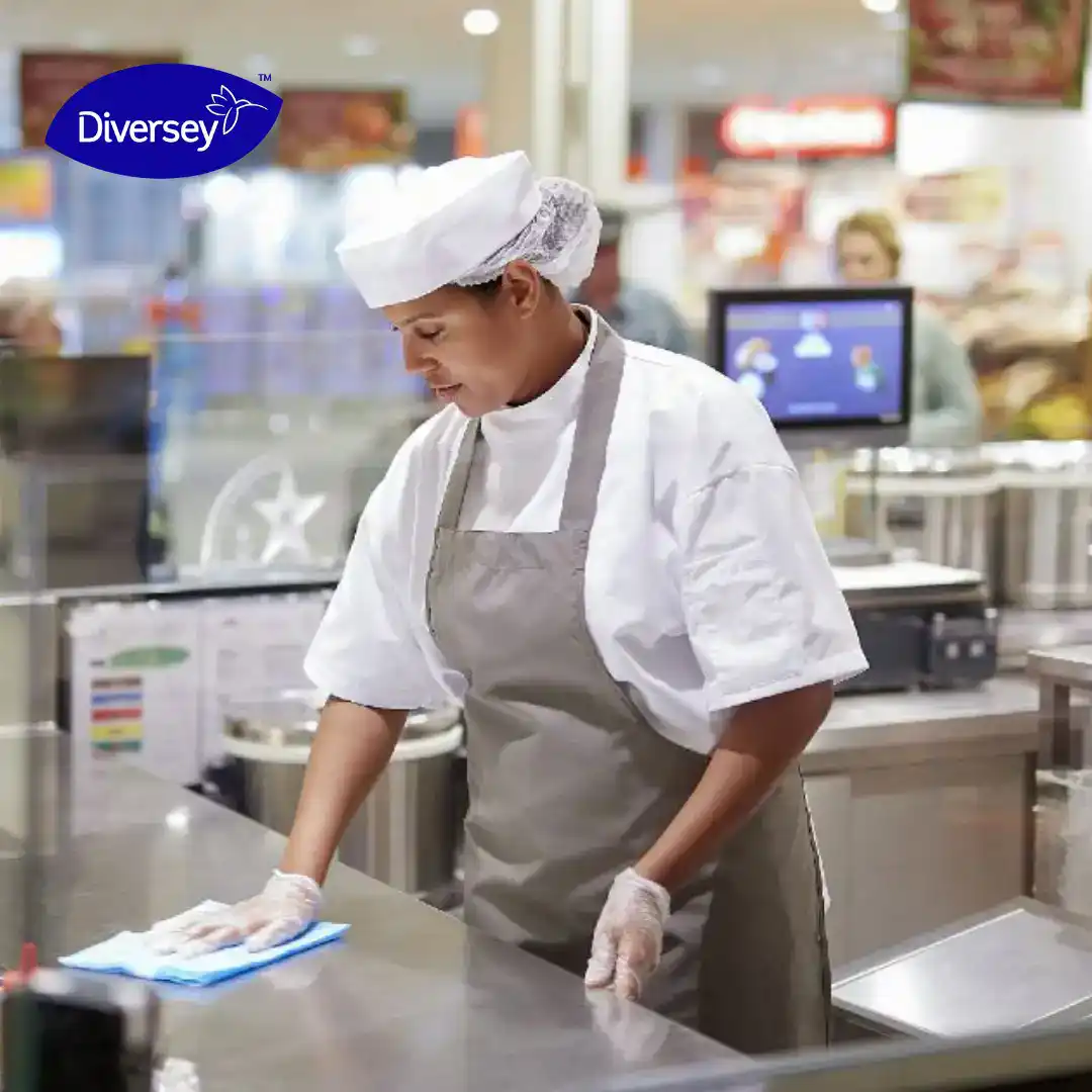 Fresh food industry worker cleaning stainless steel surface with cloth for hygiene and safety in commercial kitchen.