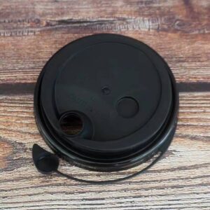Black disposable coffee cup lid with straw hole and sip hole on wooden surface.