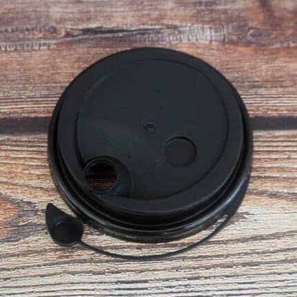 Black disposable coffee cup lid with straw hole and sip hole on wooden surface.