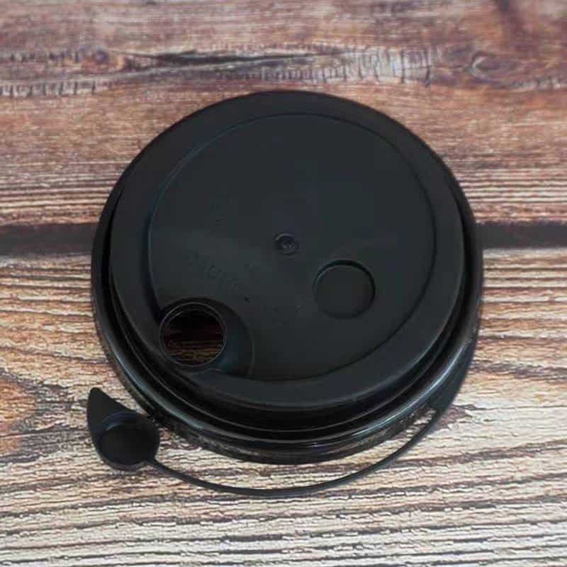 Hard Lid, Conjoined Black Black disposable coffee cup lid with straw hole and sip hole on wooden surface.